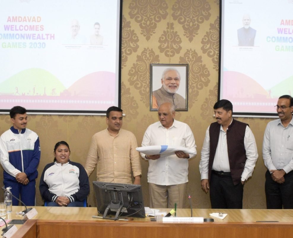 Gujarat Deputy Chief Minister Harsh Sanghavi and Chief Minister Bhupendra Patel with the Commonwealth Games Flag alongside Gujarat's athletes.