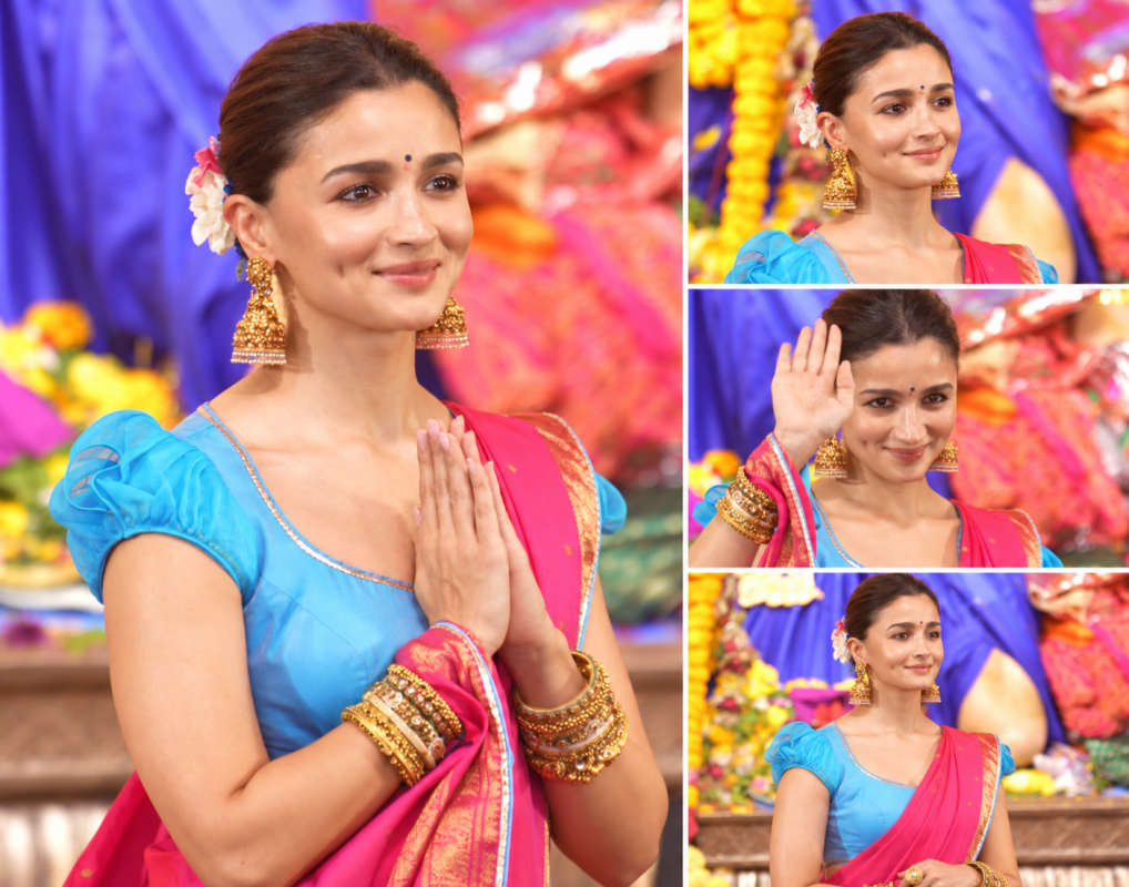 Alia Bhatt in a vibrant pink saree and blue blouse with gold jewellery and floral hair accessories during festive celebrations.